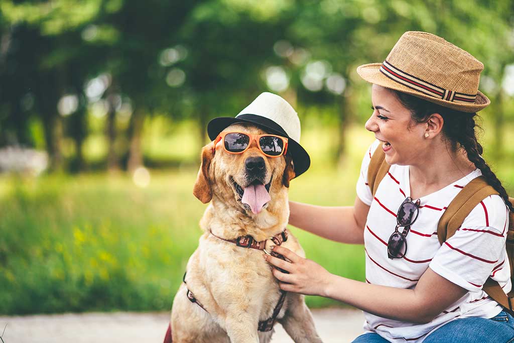 Young woman and her labrador dog having fun in nature with hats and sunglasses